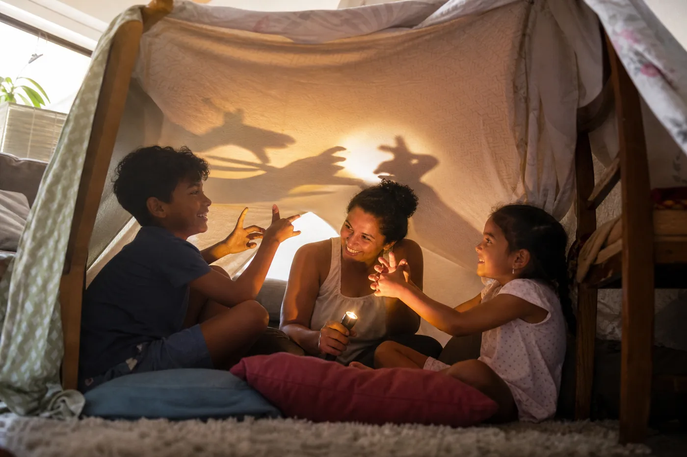 Família brincando com sombras dentro de uma cabana feita com lençóis